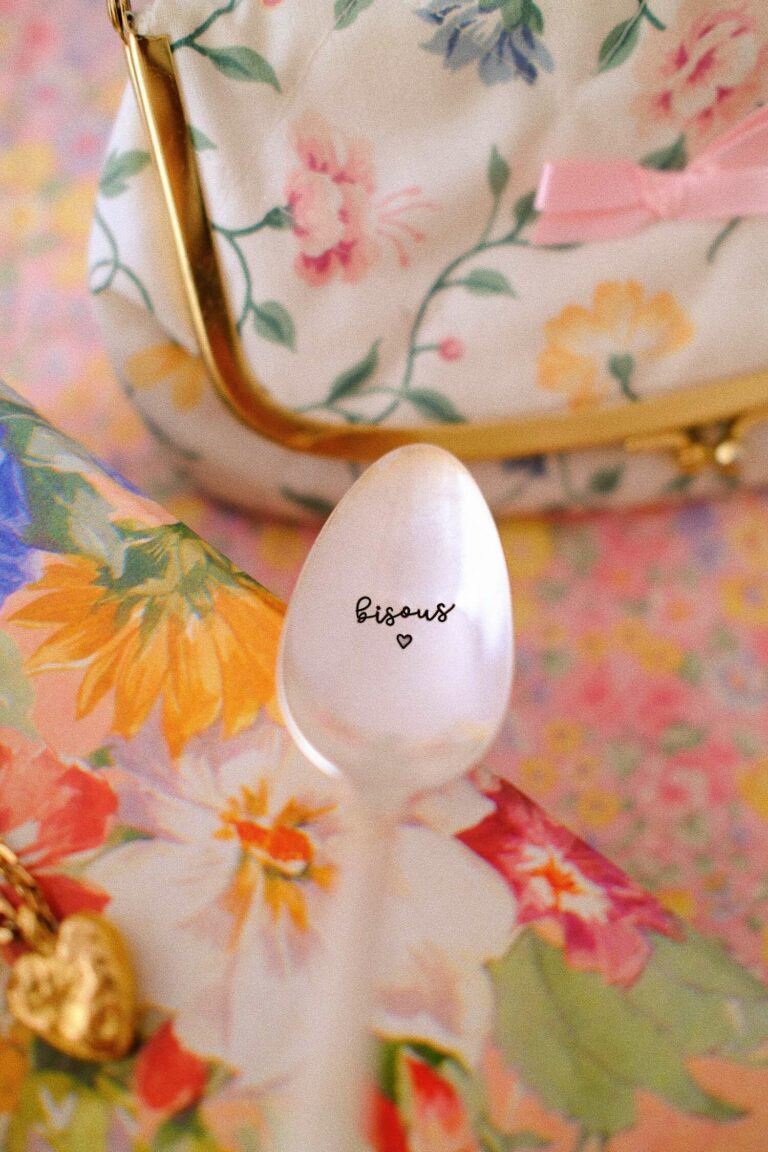Cuillère vintage gravée « Bisous », mise en scène sur un fond fleuri avec une trousse à fleurs en arrière-plan.
