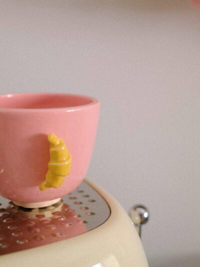 petite tasse en faïence rose avec une anse croissant jaune posée sur une machine à café