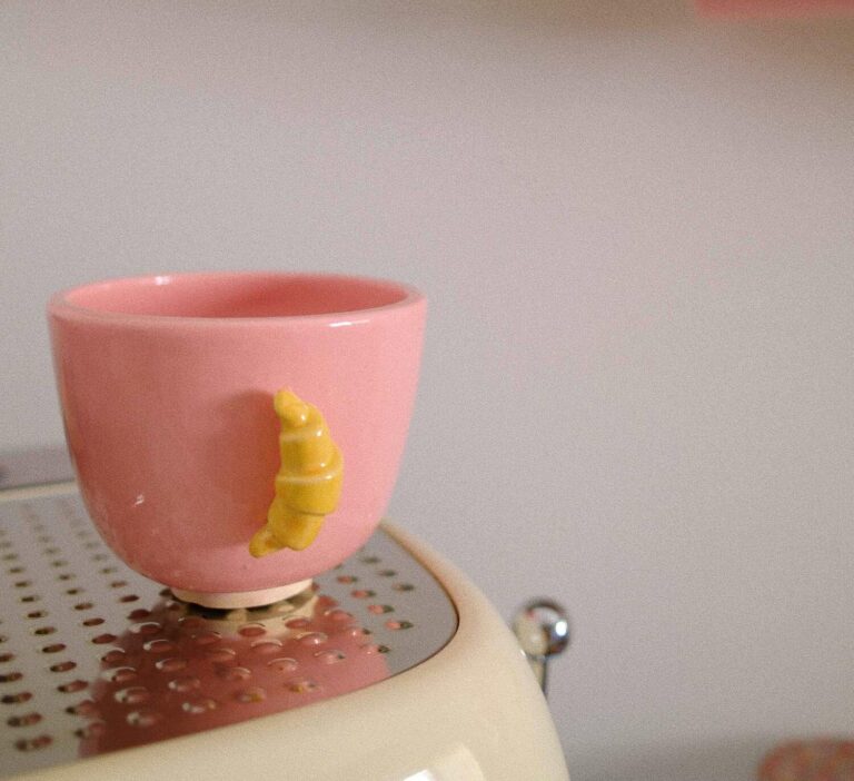 petite tasse en faïence rose avec une anse croissant jaune posée sur une machine à café