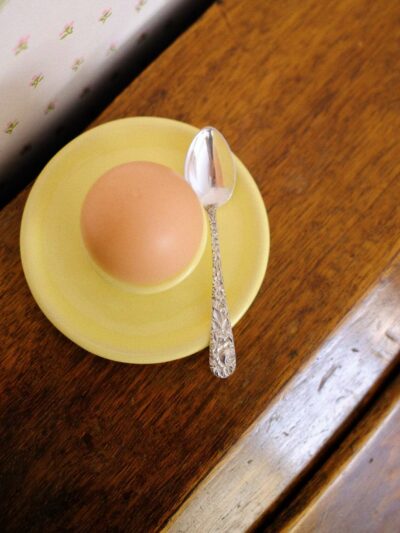 petite assiette coquetier jaune posée sur un bureau en bois avec une petite cuillère en argent posée dessus