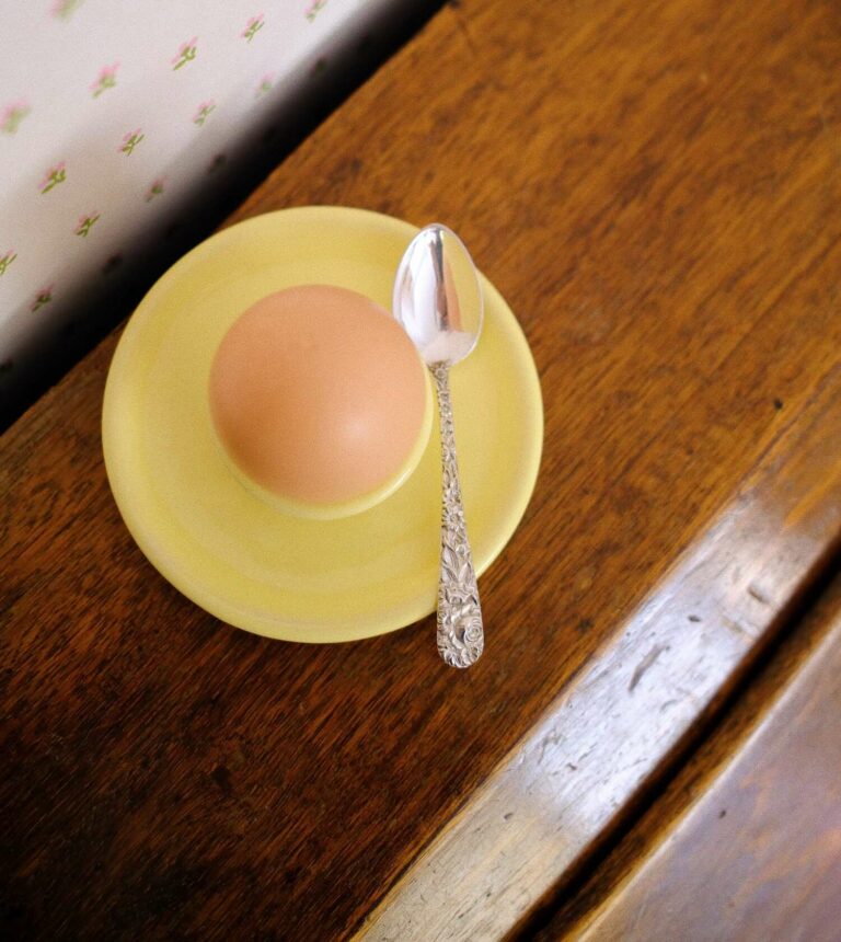 petite assiette coquetier jaune posée sur un bureau en bois avec une petite cuillère en argent posée dessus